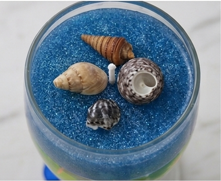 Top-down view of sapphire blue sand with hand-placed seashells inside the candle